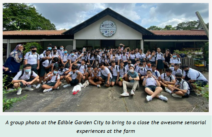 A large group of students in school uniforms posing together in front of the Edible Garden City building.